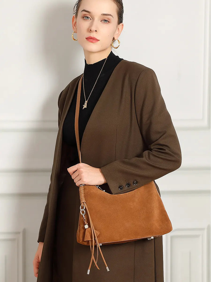 Woman holding a brown leather handbag against a white wall