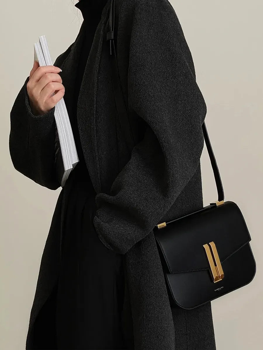 Person wearing a black coat with a black handbag on a neutral background