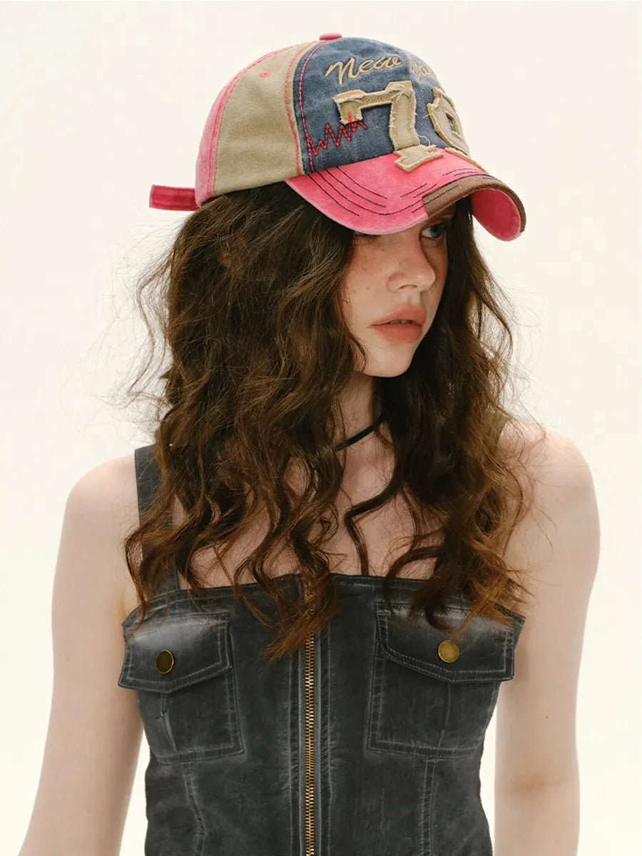 Woman wearing a colorful baseball cap with a denim dress on a plain background